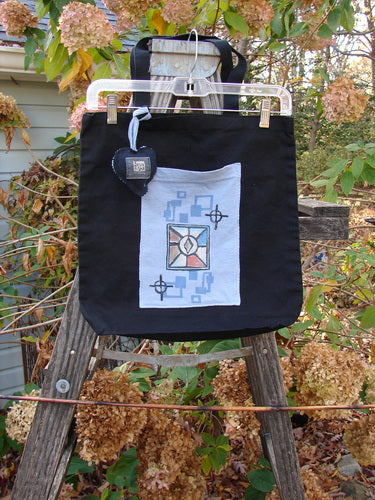 2000 PMU Patched Tote Bag Geos Black One Size, displayed on a ladder, features extra-long shoulder straps, a generous top opening, gusset bottom, and colorful accents, exemplifying Bluefishfinder.com's sustainable, artistic approach.