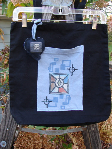 2000 PMU Patched Tote Bag Geos Black One Size hanging on a clothesline, showcasing colorful patches and a blue heart accent. The bag features long shoulder straps and a gusset bottom.