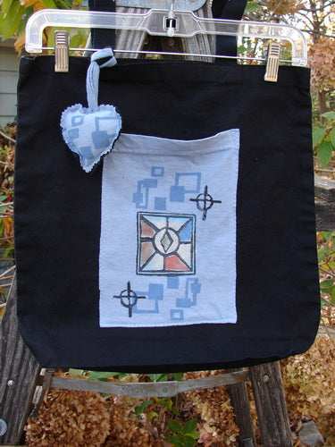 2000 PMU Patched Tote Bag Geos Black One Size hanging on a clothesline, featuring a puffy heart accent, extra-long shoulder straps, and a gusset bottom, showcasing its eco-friendly, vintage-inspired design.