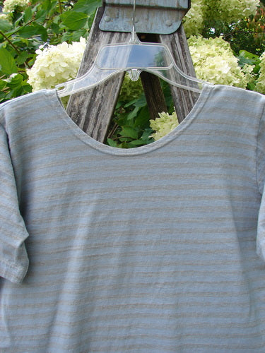 1997 Little Voyage Top in gray-blue stripe, tiny size 2, shown as a soft, lightweight knit with a rounded neck and short sleeves. The striped fabric hangs on a clear hanger against weathered wood and pale hydrangeas.