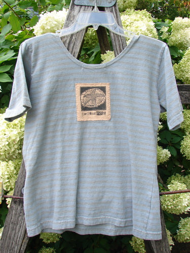1997 Little Voyage Top in gray-blue stripes, tiny size 2, shown as a softly draped short-sleeve T-shirt with a scoop neckline and a small centered chest patch graphic. The lightweight knit hangs from a hanger, with pale horizontal striping and a casual, worn-in finish.