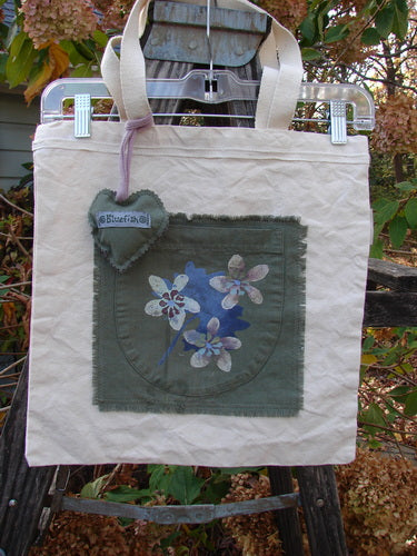 2000 PMU Patched Organic Cotton Canvas Pocket Tote Bag Frayed Floral Natural One Size, featuring a blue flower design, tightly woven shoulder straps, and a heart-shaped puffy charm, celebrating sustainable vintage design.