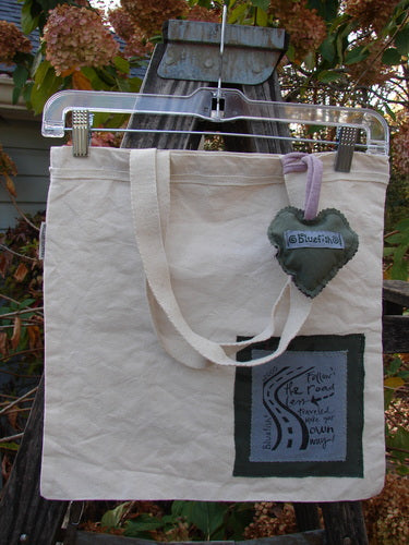 2000 PMU Patched Organic Cotton Canvas Pocket Tote Bag features a heart-shaped charm and fringe accents, showcasing vintage-inspired floral detailing and sustainable design from Bluefishfinder.com.