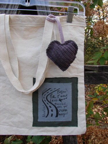 2000 PMU Patched Organic Cotton Canvas Pocket Tote Bag features a purple heart charm on a clothespin, showcasing the PatchMeUp program's vintage-inspired design with floral accents and fringe detail.