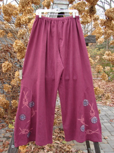 A pair of purple pants with a flower design and unique side panel insert. Full elastic waistline, widening lowers, and lower circle floral paint. No pockets. Size 2.