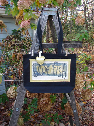 1995 PMU Patched Tote Bag Sling displayed on a wooden ladder, showcasing its vintage logo and frayed detailing. Features include long shoulder straps and a colorful heart accent.