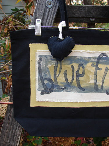 1995 PMU Patched Tote Bag Sling featuring a black canvas with yellow accents, adorned with a colorful heart and signature patch, emphasizing vintage style and sustainability from Bluefishfinder.com.