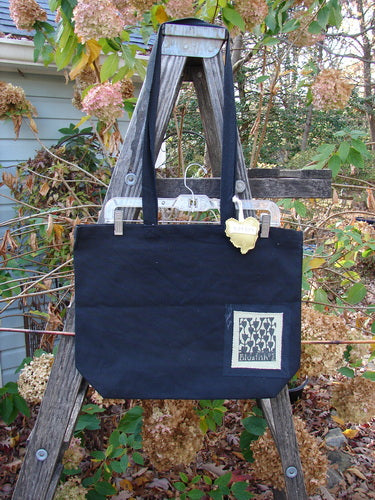 1995 PMU Patched Tote Bag Sling Vintage Logo Frayed Black Yellow One Size displayed on a wooden ladder, showcasing its long shoulder straps, generous top opening, and colorful puffy heart accent.