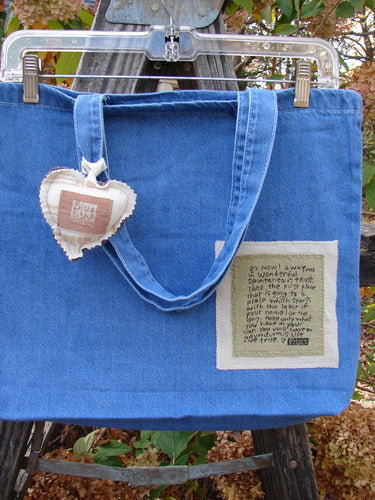 2001 PMU Patched Tote Bag Summer Frayed Logo Washed Denim One Size, featuring a colorful puffy heart accent, tote-length shoulder straps, and a gusset bottom, displayed outdoors with a plant backdrop.