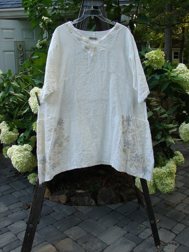 Barclay Linen Cross Over Urchin Tunic Dress Daisy Cloud Size 2 on a rack, featuring a V-neckline, drop shoulders, double side pockets, and a daisy floral pattern.