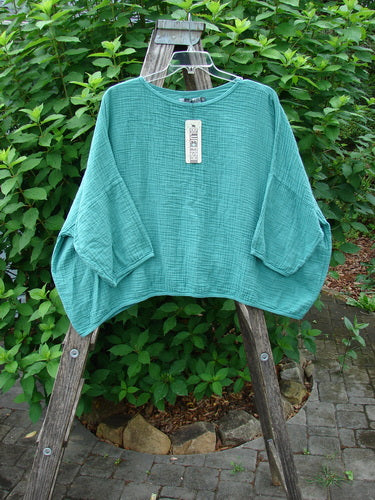 Barclay NWT Gauze Square Mariposa Pullover Unpainted Jade OSFA displayed on a wooden ladder, showcasing its textured cotton gauze, wide sleeves, and boxy flowy shape, suitable for creative spring layering.