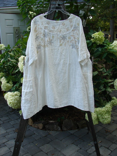 Barclay Linen Cross Over Urchin Tunic Dress Daisy Cloud Size 2 on a clothes rack, showcasing its V neckline, drop shoulders, and daisy-themed design.