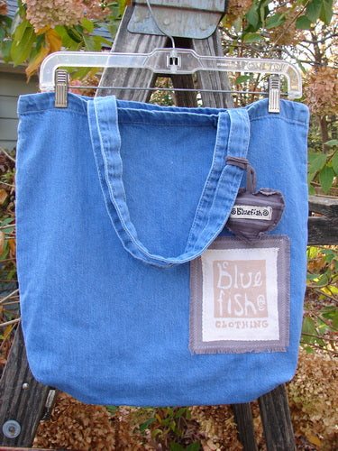 2000 PMU Patched Cotton Pocket Tote Bag Frayed Daisy Washed Denim One Size, featuring a heart-shaped charm and Blue Fish patch, displayed hanging, showcasing its recycled vintage design by Bluefishfinder.com.