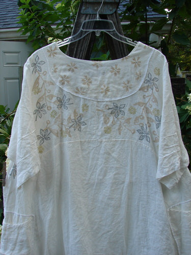 Barclay Linen Cross Over Urchin Tunic Dress Daisy Cloud Size 2 displayed on a hanger, showcasing a floral design with a V neckline and varying side lengths.