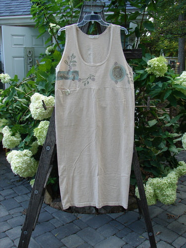 1995 Tab Jumper Magic Forest Natural Altered OSFA: A white organic cotton dress on a wooden rack featuring an extreme scoop neckline, tiny pocket with a blue ceramic button, and a painted rear tab.