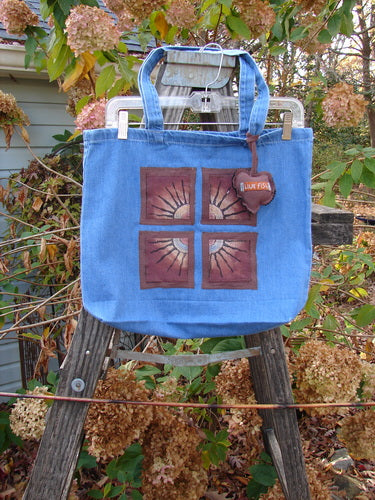 1998 PMU Patched Tote Bag Fall Quad Washed Denim One Size, featuring a brown heart patch, blue strap, and gusset bottom, displayed on a ladder, highlighting sustainable vintage design by Jennifer Barclay.