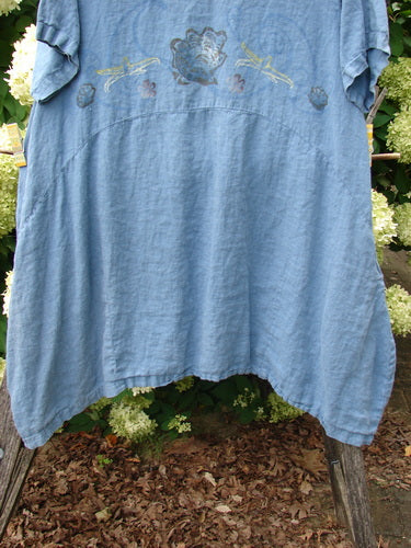 1997 Urchin Dress Floral Starfish Naya Size 1 in faded blue fabric, with embroidered floral and starfish motifs across the chest and a softly draped, loose silhouette. The textured dress hangs outdoors against leafy greenery, with ruffled sleeves and an uneven hem.