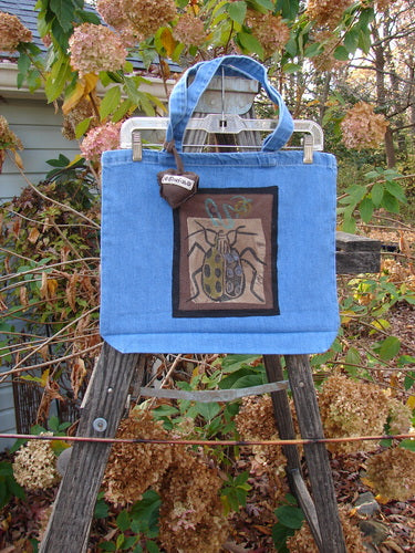 1996 PMU Patched Tote Bag Beetle Washed Denim One Size, displayed on a ladder with a distinct beetle patch, showcasing tote length shoulder straps and a generous top opening.