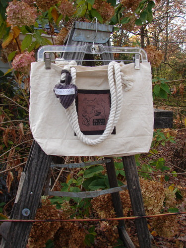 1998 PMU Patched Canvas Rope Pocket Tote Bag Ash Leaf Natural One Size on a wooden ladder, featuring cotton rope straps, a heart tag, and a Blue Fish patch, emphasizing sustainable vintage design.