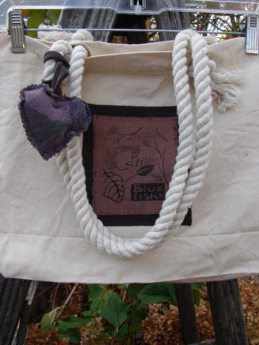 1998 PMU Patched Canvas Rope Pocket Tote Bag Ash Leaf Natural One Size, showcasing a white rope detail and pink patch, hanging on a clothesline with plant elements in view.