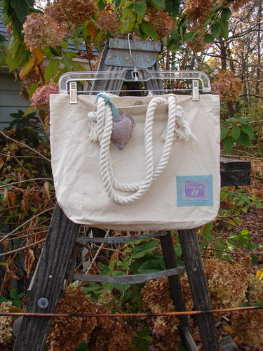 Barclay PMU Patched Canvas Rope Pocket Tote Bag Butterfly Natural One Size hangs on a wooden ladder, showcasing its rope handles and unique vintage patches, embodying Bluefishfinder.com's sustainable and creative ethos.