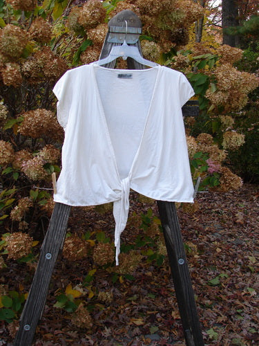 A white cotton lycra cap sleeve tie shrug displayed on a rack.