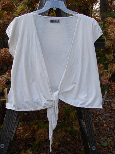 A white cotton lycra cap sleeve tie shrug hanging on a clothesline.