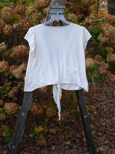 A white cotton lycra cap sleeve tie shrug displayed on a wooden rack, showcasing its sectional straight panels and raw edges.