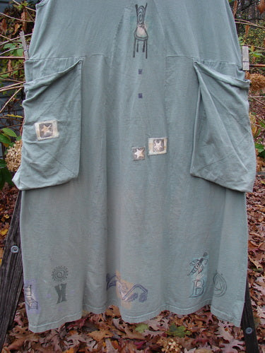 1994 PMU Patched Cross Smock in Seaweed, featuring oversized stitched pockets, a deep V-neckline, and star patches, displayed on a clothes rack, highlighting its vintage charm and unique design.