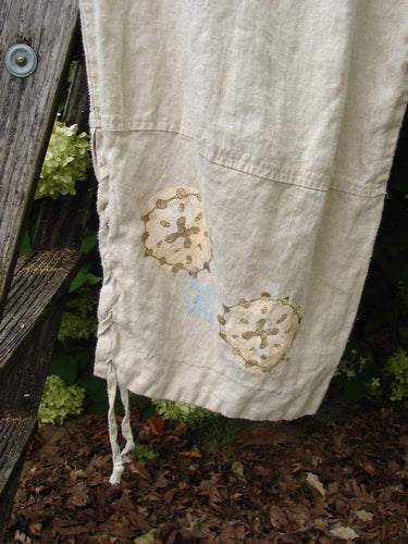1997 Skipper Pant Rolling Sealife Natural Size 1 in natural linen, shown as loose beige pants with a soft woven texture, seam detailing, and two shell-like sealife motifs near the hem; thin ties hang at the lower edge.