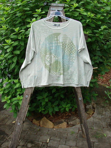 Barclay Cricket Cap Sleeve Tee Centered Dune Grass OSFA displayed outdoors, showcasing its cap sleeves, seamless shoulder, and boxy shape, emphasizing the organic cotton's texture and unique design elements.