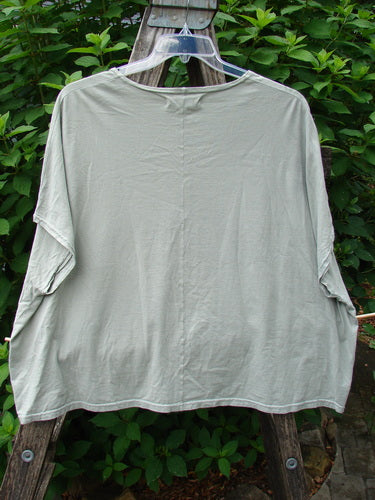 Barclay Cricket Cap Sleeve Tee Centered Dune Grass OSFA displayed on a clothes rack, showcasing its cap sleeves, rounded hemline, and boxy shape, highlighting its lightweight organic cotton fabric and seamless shoulder design.