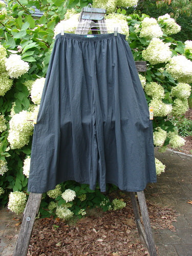 Barclay Batiste Crop Wide Leg Pant in unpainted black, size 2, with a voluminous wide-leg silhouette and gathered elastic waistband. The lightweight fabric drapes from a wooden ladder outdoors, framed by dense white hydrangeas and green foliage.
