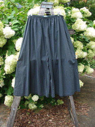 Barclay Batiste Crop Wide Leg Pant in unpainted black, size 2, with a relaxed wide-leg silhouette and cropped length. The lightweight woven fabric hangs from a simple gathered waistband, displayed outdoors against green foliage and white hydrangeas.