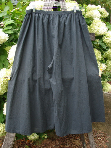 Barclay Batiste Crop Wide Leg Pant in unpainted black, size 2, with a loose, airy silhouette and softly crinkled fabric. The wide legs hang from an elastic waistband, shown on a hanger against leafy white hydrangeas and greenery.