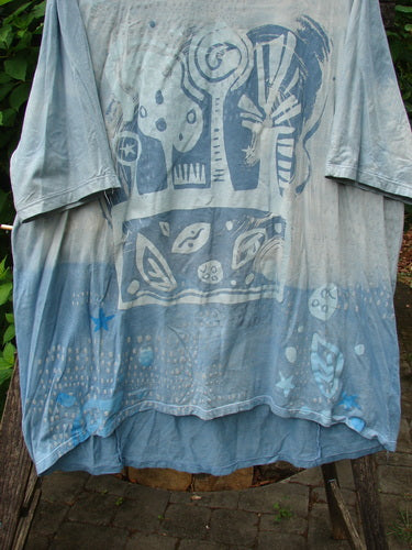 Barclay Tournesol Tunic Flower Power Mottled Day Sky OSFA displayed outdoors, showcasing its loose three-quarter sleeves, rounded neckline, varying hemline, and distinctive flower power design.