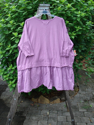 Barclay Batiste Banded Flounce Esperanza Tunic Sprig Crocus OSFA hanging on a clothes rack, showcasing its dolman sleeves, rounded neckline, and varying hem in a relaxed, boxy shape.