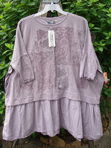 Barclay NWT Batiste Banded Flounce Esperanza Tunic features a rounded neckline, Dolman sleeves with lettuce edges, and a floral theme on a purple fabric, displayed with a visible tag.