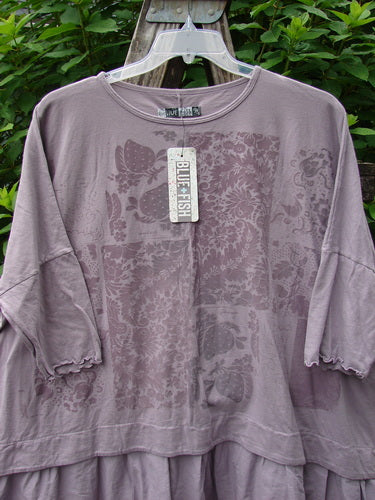 Barclay NWT Batiste Banded Flounce Esperanza Tunic Garden Sea Fog OSFA displayed on a hanger, highlighting its distinctive dolman sleeves with lettuce edges and a floral-themed design, embodying a unique, artistic style.