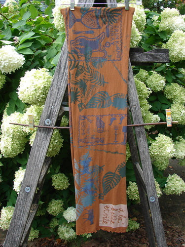 Barclay Curly Edge Center Seam Scarf Wrap in rust, a long rectangular scarf with curly edges and a center seam, printed with blue leafy and bird motifs. It hangs vertically on a wooden ladder, with a pale woven end panel.