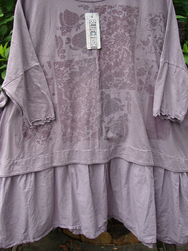 Barclay NWT Batiste Banded Flounce Esperanza Tunic Garden Sea Fog OSFA displayed on a hanger, featuring dolman sleeves with lettuce edges, a wide boxy shape, and a floral painted theme.
