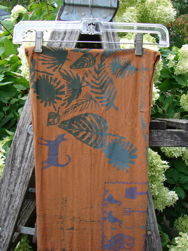 Barclay Curly Edge Center Seam Scarf Wrap in Fall Forest Friend Rust OSFA, a rust-colored scarf with teal and navy leaf and fern prints, clipped to a clear hanger. The lightweight fabric hangs in a long vertical panel with a center seam and softly curved edge detail.