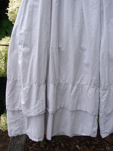 Barclay Batiste Cotton Wide Leg Carassai Pant in unpainted stone, size 2, shown in lightweight cotton with a softly crinkled texture and wide, flowing legs. The hem falls in layered panels, with a pale gray tone against a leafy outdoor backdrop.