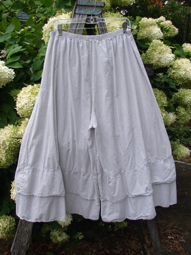 Barclay Batiste Cotton Wide Leg Carassai Pant in Unpainted Stone, size 2, shown as airy cotton wide-leg pants with a gathered elastic waist and layered hem. The pale stone fabric hangs softly from a clear hanger against leafy greenery, with a lightly crinkled texture and relaxed drape.