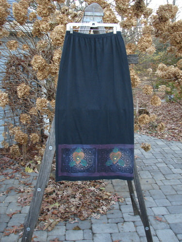 1999 Vented Straight Duo Heart Black Size 1: A skirt on a wooden stand, featuring a black design with colorful mosaic hearts. Made from organic cotton, this skirt is from the Winter Collection of 1999. Perfect condition.