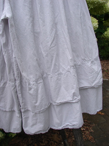 Barclay Batiste Cotton Wide Leg Carassai Pant in unpainted stone, size 2, with a soft crinkled cotton texture and layered wide-leg hem. The pale gray fabric falls in voluminous folds against an outdoor backdrop of greenery and stone.