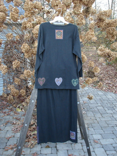 1999 Vented Straight Duo Heart Black Size 1: Long sleeve black shirt and matching skirt on a wooden stand. Shirt features rolled neckline, vented sides, and colorful mosaic heart paint. Skirt has elastic waist and colorful mosaic hearts. Perfect condition, made from organic cotton. Winter Collection.