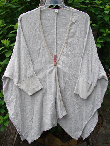 Barclay Gauze Open Front Cardigan Unpainted Natural Size 2, displayed on a wooden pole, highlights dolman sleeves and contrasting cuffs, embodying Blue Fish Clothing's creative and vintage style.