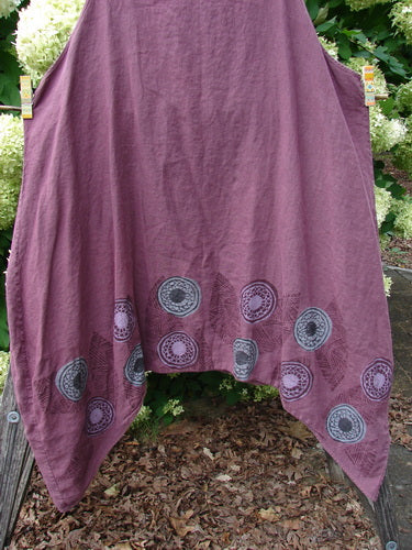 Barclay Linen Flared Pinafore Shift Dress Pinwheel Turn Leaf Berry Size 2 in berry linen, with a softly draped A-line shape and rounded hem. Circular pinwheel turn leaf motifs border the lower edge, while the fabric’s textured weave and muted finish create a layered, earthy look.