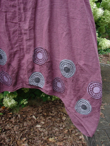 Barclay Linen Flared Pinafore Shift Dress Pinwheel Turn Leaf Berry, size 2, in berry linen with a softly flared hem. The fabric shows a textured weave and scattered circular pinwheel motifs in muted gray and lavender, draping over leafy ground.